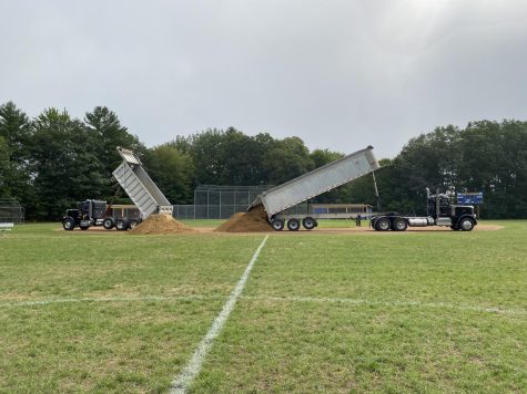 Two large dump trucks spill out new material on the BMU Baseball field. 