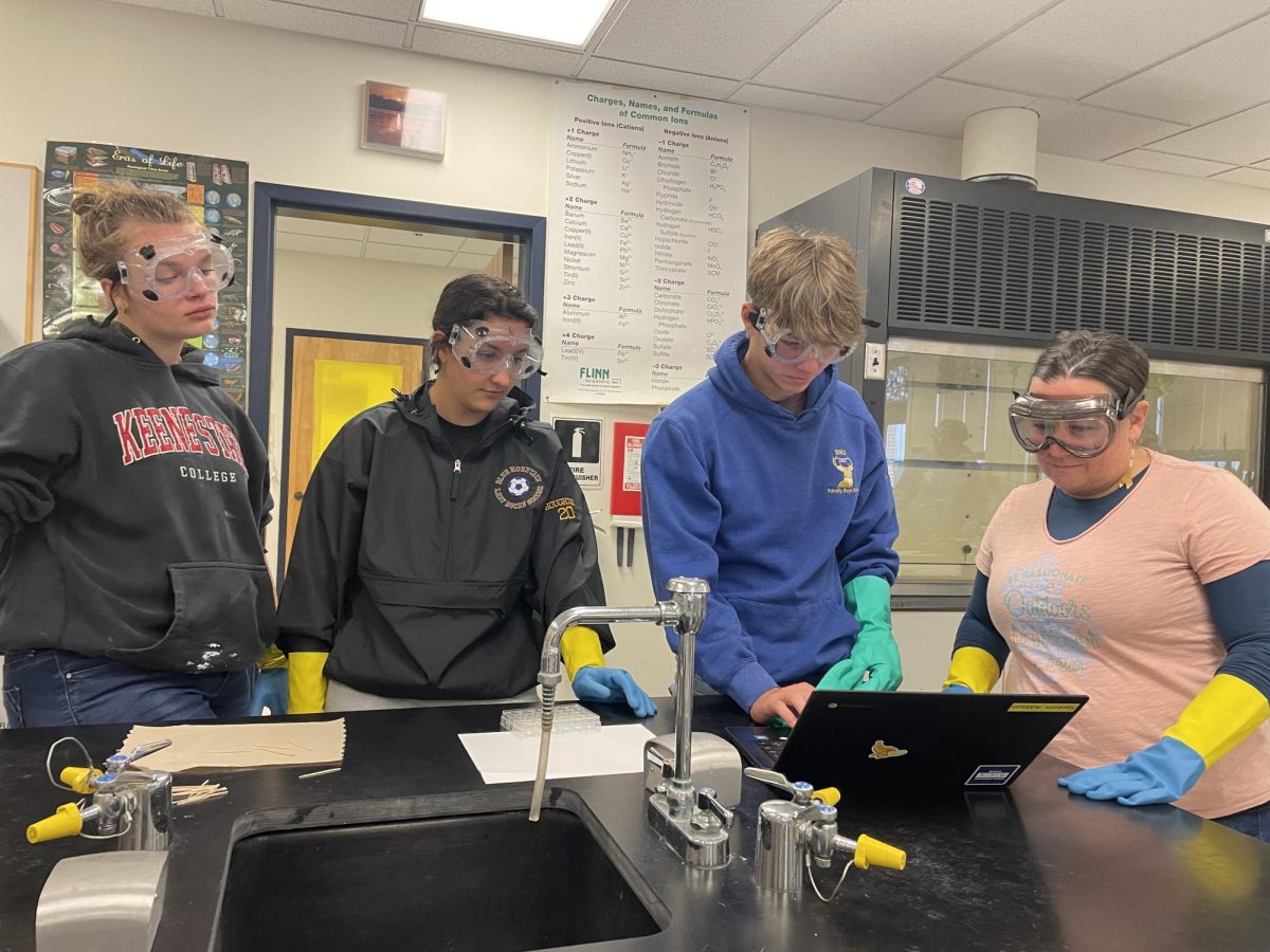 On November 7th, 2023 high school science teacher Kimberly Adams helps honors chemistry students Maddison Fellows (11th grade), Madalyn Houghton (11th grade), and Addison Sanborn (11th grade) with a hands-on experiment, practicing naming & forming ionic compounds.