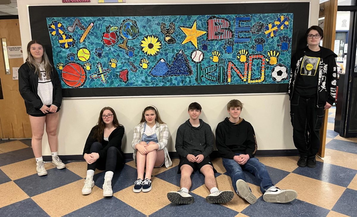 The BMU high school studio art class is seen here on Monday, April 9, 2024, posing In front of a recently finished mosaic piece representing Blue Mountain. This piece is currently on the bulletin board in front of the art room but will be moved to the cafeteria.