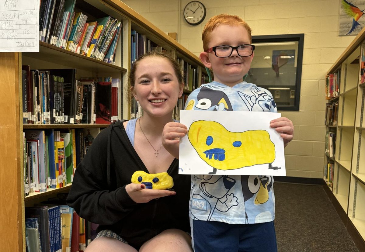 BMU Studio Art student Bella Craige is seen here with first grader Jaxson Carle on Friday, May 17, 2024 holding the art project they have been working on recently. The Studio Art class took on the project to recreate the monster drawings of first grade students. 