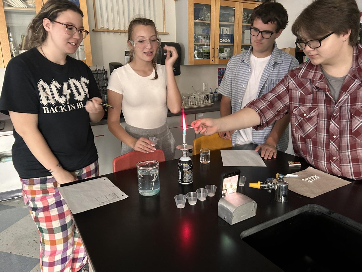 High school sophomores Izzy Florentine (Left), Tori Florentine (Middle) and Colby Daily (Right), watching sophomore Hunter Fisher light a cotton swab dipped in lithium and strontium on fire to emit a red flame, on October 2, in Mrs. Adam's high school chemistry classroom. The students are looking at the color different elements produce when heated in a flame. 